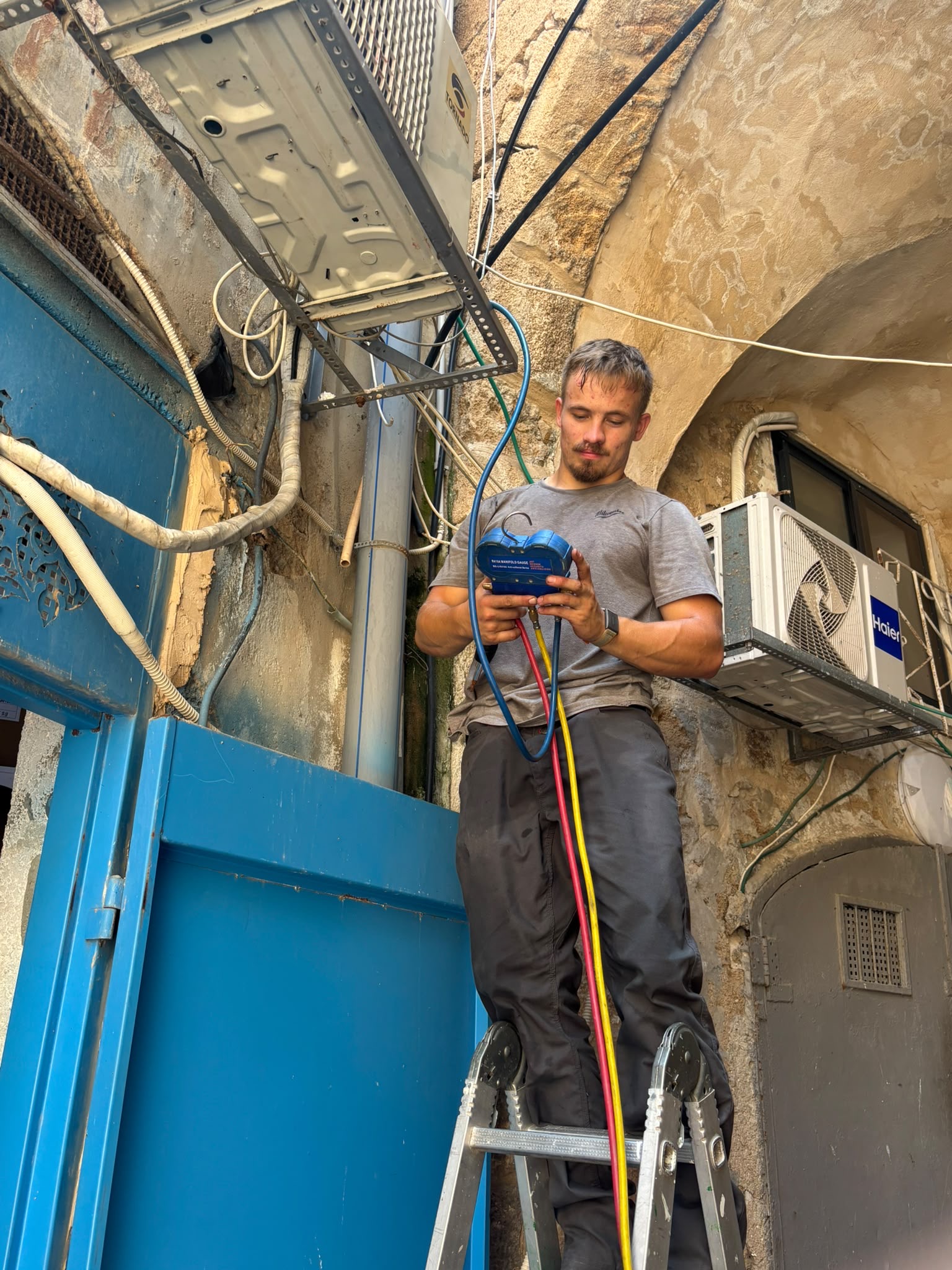 טכנאי מבצע בדיקת לחץ גז במזגן מיני-ספליט על סולם