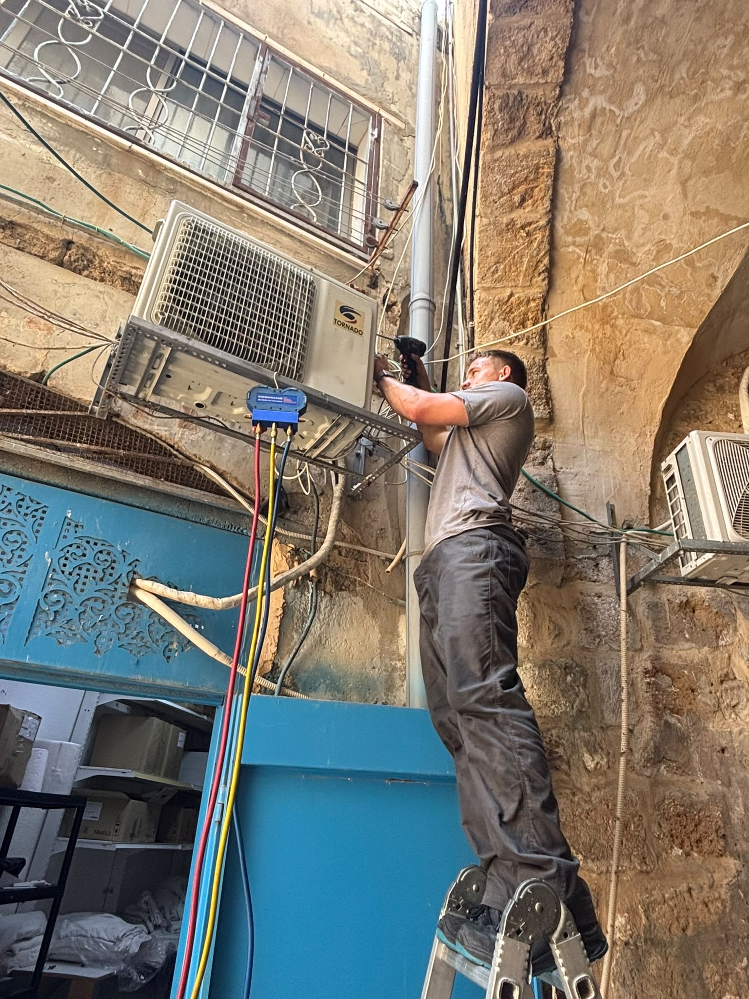 טכנאי מתקין יחידת עיבוי חיצונית של מזגן על חזית מבנה